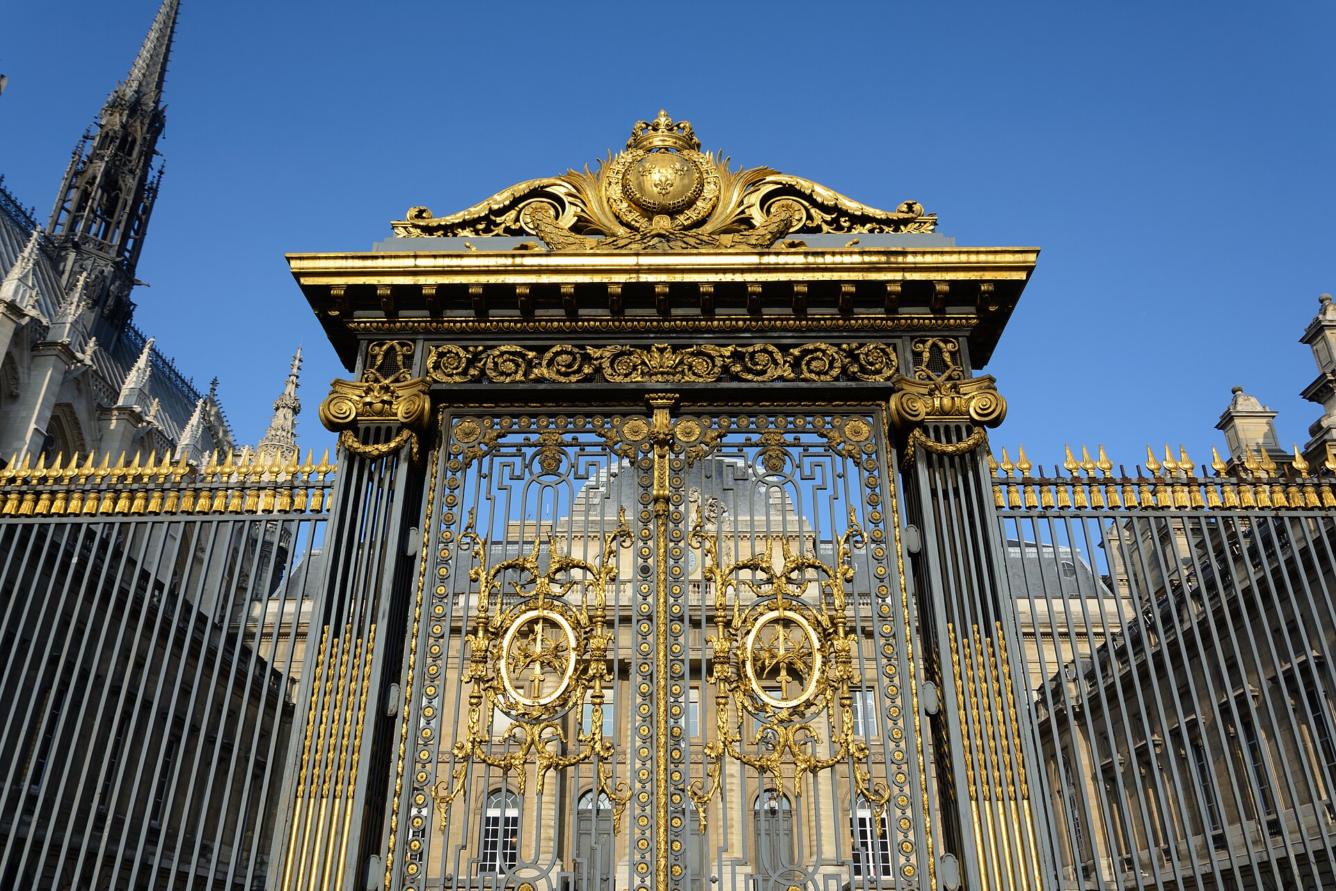Grille dorée et ornée à l’entrée d’un palais de justice sous un ciel bleu